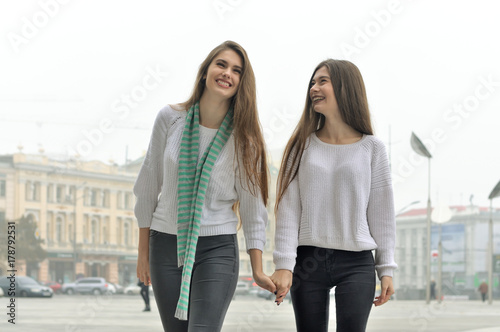 Two girlfriends are walking through the city, holding hands and laughing