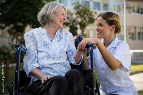 Doctor talking to woman sitting on wheelchair in park