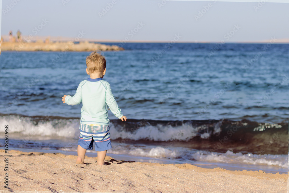 Back view of toddler in swimming suit running to the the sea. Copy space