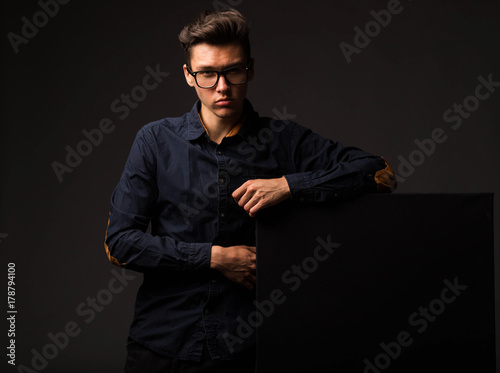 Young confident man portrait of a businessman showing presentation, pointing paper placard black background. Ideal for banners, registration forms, presentation, landings, presenting concept.