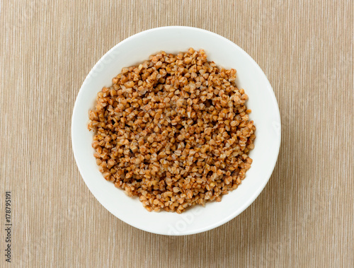 Buckwheat porridge in a white plate on textured background. Top view, closeup.