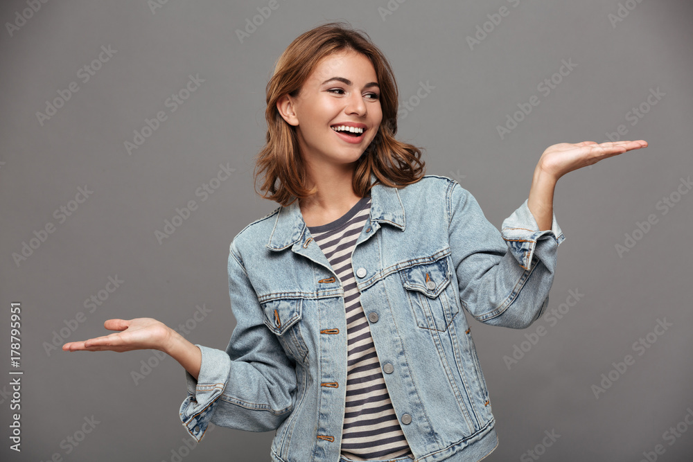 Young cheerful woman in jeans jacket looking at her empty palm Young cheerful woman in jeans jacket looking at her empty palm
