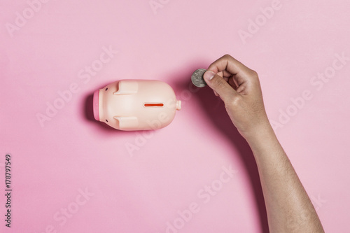 hand hold coin into coin bank on the pink background.