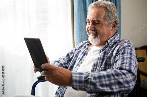 Smiling senior man using digital tablet by sitting on wheelchair