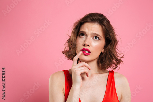 Close-up portrait of thinking young beautiful woman with red lips, touching with finger her cheek, looking upward