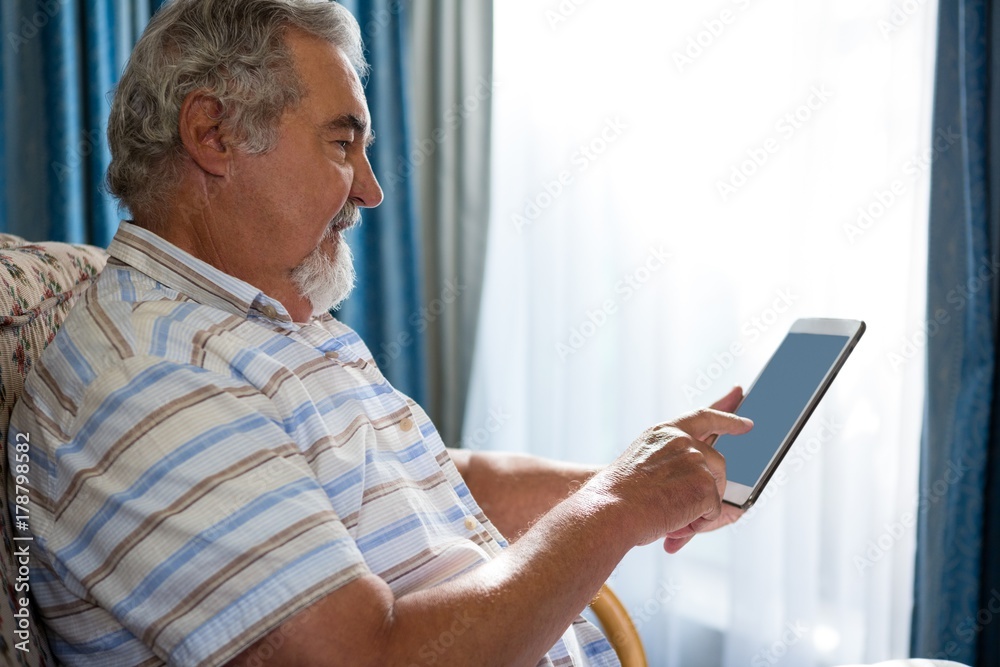 Side view of senior man using digital tablet while sitting on