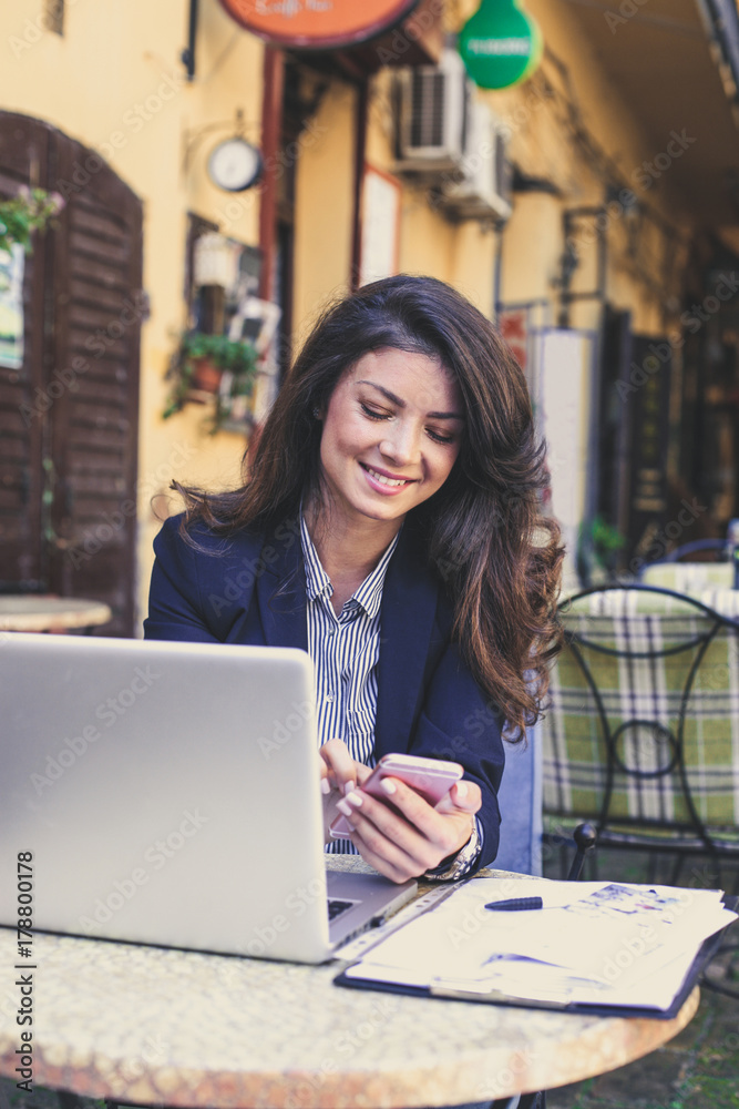 Happy young business woman working at cafe, using mobile phone.