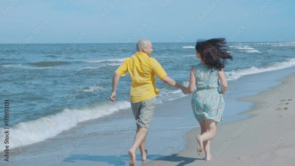 Happy lovely couple running along the seacoast barefoot and enjoys herself. Beach with white sand. Outgoing coastal line. Slow Motion. Happy lovely couple running along the seacoast barefoot and enjoys herself. Beach with white sand. Outgoing coastal line. Slow Motion.