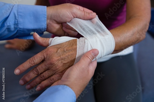 Canvas Physiotherapist putting bandage on injured hand of patient