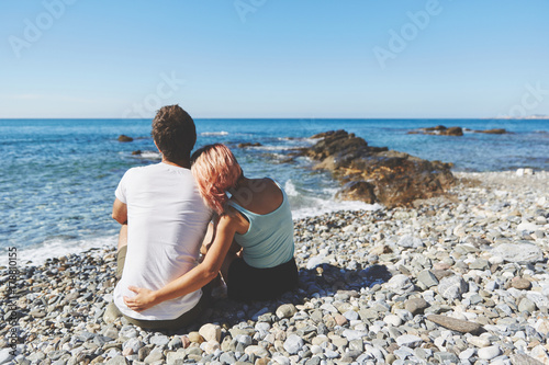 Couple sitting on rocky beach looking at sea