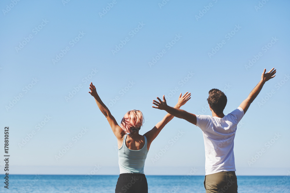 Man and woman raising hands looking at sea Man and woman raising hands looking at sea