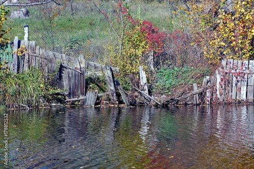 сломанный заросший деревянный забор в растительности в воде