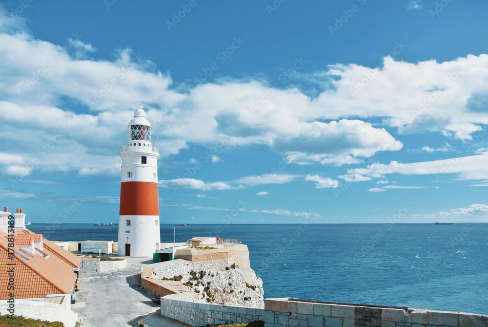 A view of beautiful red and white Trinity Lighthouse, orange tile roofs and vivid blue water at Europa Point at Gibraltar, the meeting point of Mediterranean Sea and Atlantic Ocean, United Kingdom.