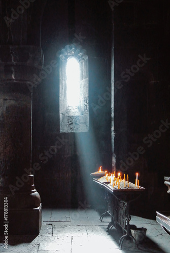 A dark background of old Armenian christian church monastery interior with a sun ray falling to the candles from a window. Abstract christian religion belief and travel concept.