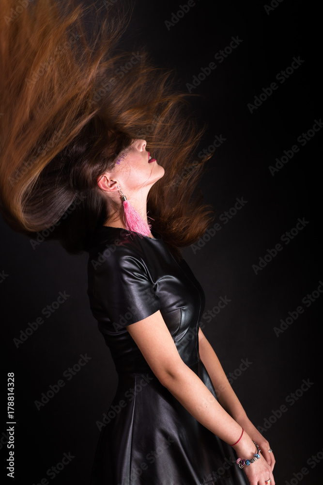 Indoors portrait of attractive young woman with makeup wearing black leather dress. Half-length falling back. Flying long beautiful hair. Dark background. Indoors portrait of attractive young woman with makeup wearing black leather dress. Half-length falling back. Flying long beautiful hair. Dark background.