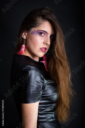 Indoors portrait of attractive young woman with makeup wearing black leather dress. Half-length. Dark background.