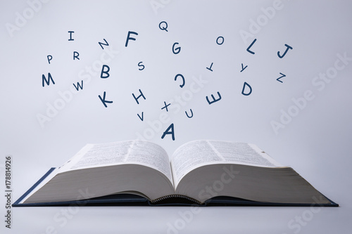 English dictionary with letters flying out of it on a white.
 photo