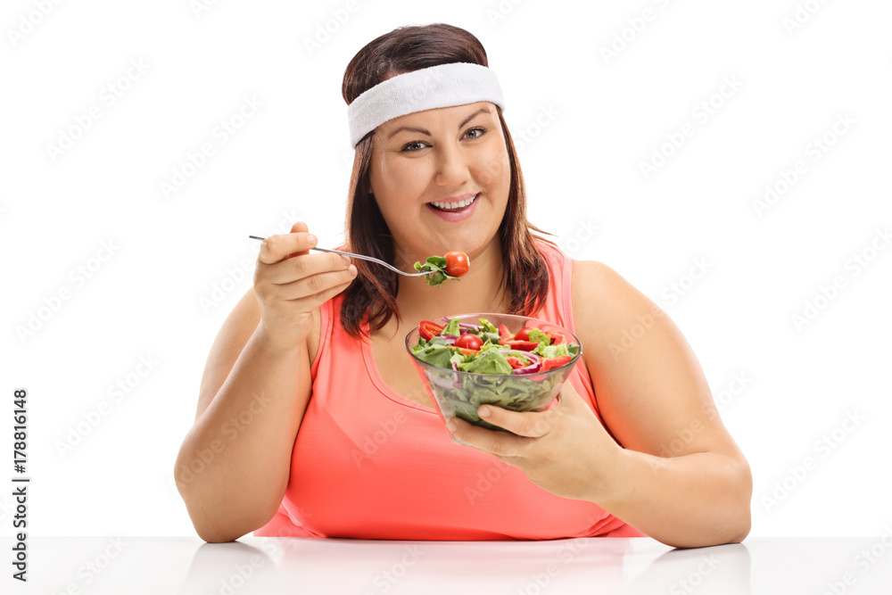 Overweight woman sitting at a table and eating a salad Overweight woman sitting at a table and eating a salad
