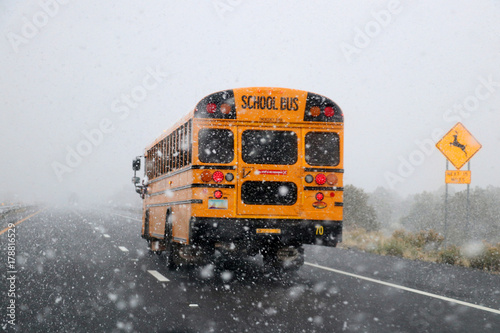 School bus in snow storm. Yellow classic school bus rides on the road during a sudden snowfall. Bad weather background. Danger concept.