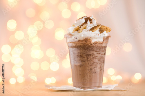 Banana cocoa in a plastic beaker to take out. Chocolate banana smoothie in glass with paper straw on wooden background, selective focus, horizontal, toned