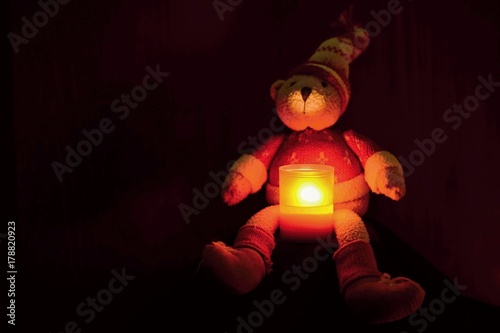 Beautiful Christmas teddy bear sitting with candle. Seasonal winter background for Christmas and holidays. Black clean background with copy space.