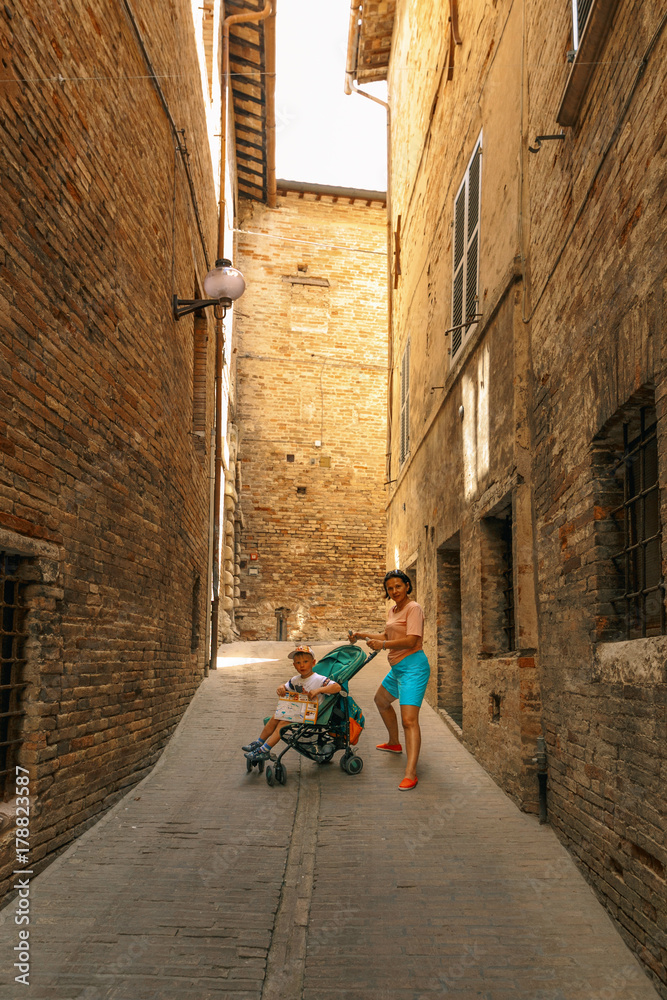 A woman with a baby stroller in the narrow street of Italy.