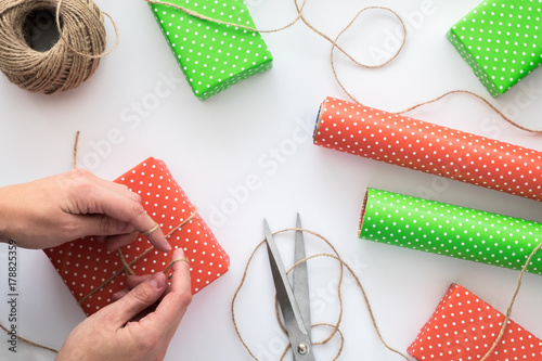 Process of package and wrapping Christmas and New Year gift box with woman hands. Wrapping paper, scissors, twine on the white background.