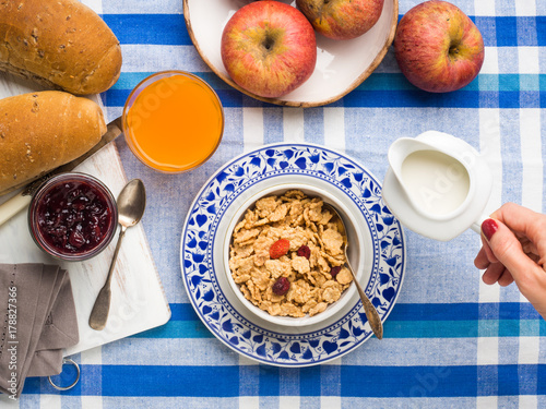 Home breakfast with cereals, milk, fruit and bread served on blue and white table cloth.