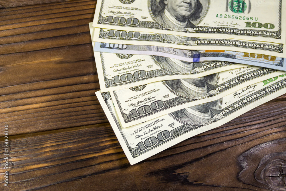 One hundred dollars bills on wooden desk One hundred dollars bills on wooden desk