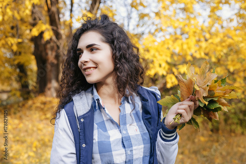 Pretty girl holding in hands bunch of leaves. Young woman looking sideways and smile. Outdoor. Close up. Autumn.