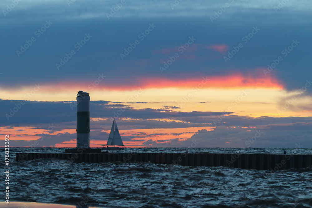 Beautiful sunset sky with pier and sailboat.