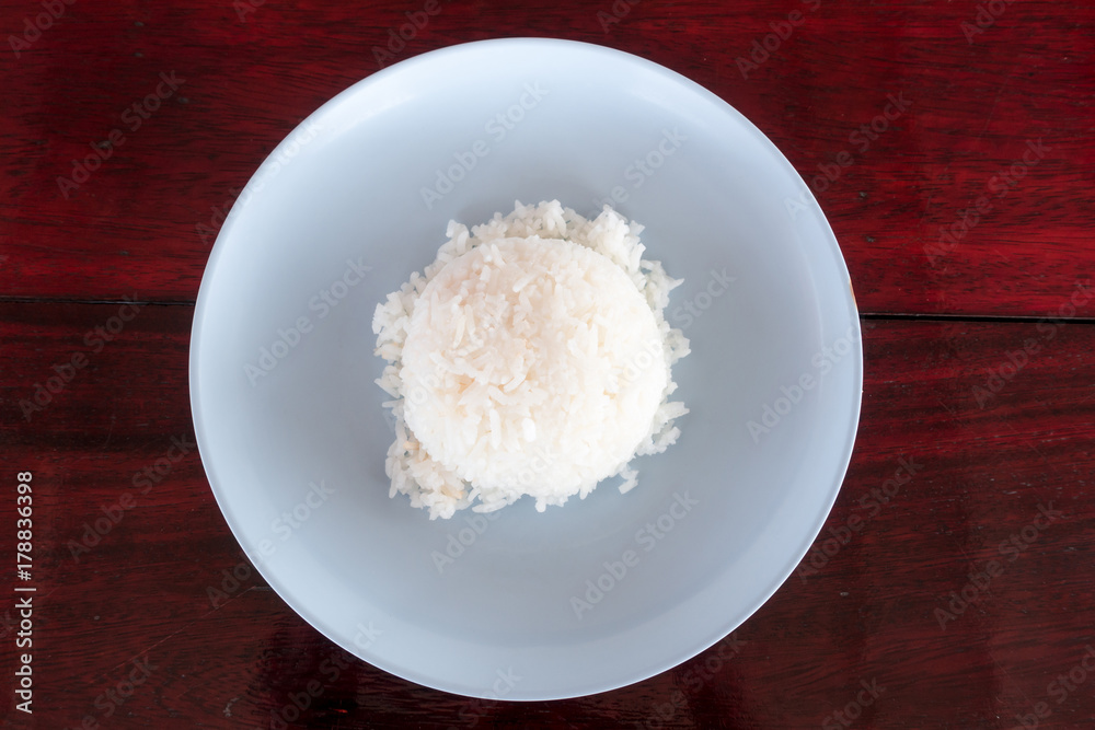Authentic freshly cook Thai jasmine rice on plastic plate on red wooden dinner table top down view. Authentic freshly cook Thai jasmine rice on plastic plate on red wooden dinner table top down view.
