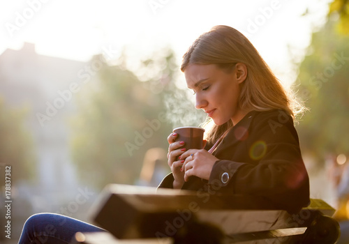 Billede på lærred Woman smelling and drinking hot coffee, autumn sunset at the street