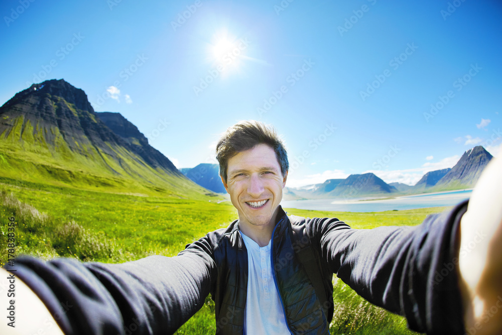 Man traveler makes selfie photo on background of mountains, fjord and sea of Iceland. man on the road thru a mountain pass, fjord is on background