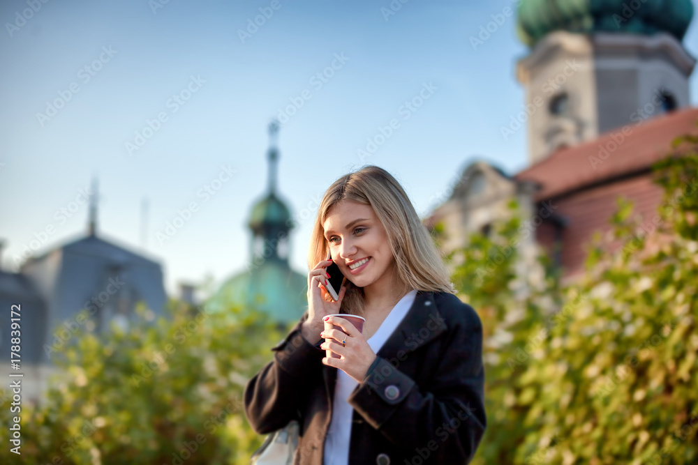 Fototapeta premium Girl with coffee cup talking on the phone and walking at the street