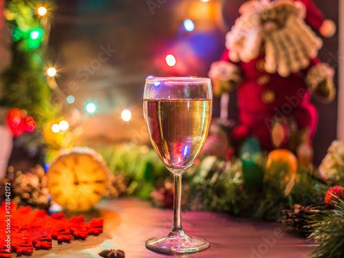 Новогодние декорации. На столе, украшенном новогодними гирляндами и Санта Клаусом, стоят деревянные часы и бокал шампанского