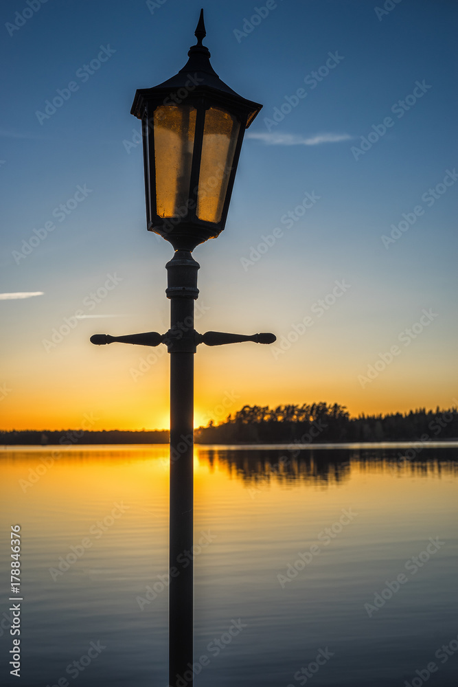 Picture of old lantern on the wooden pir and sunset at the background.