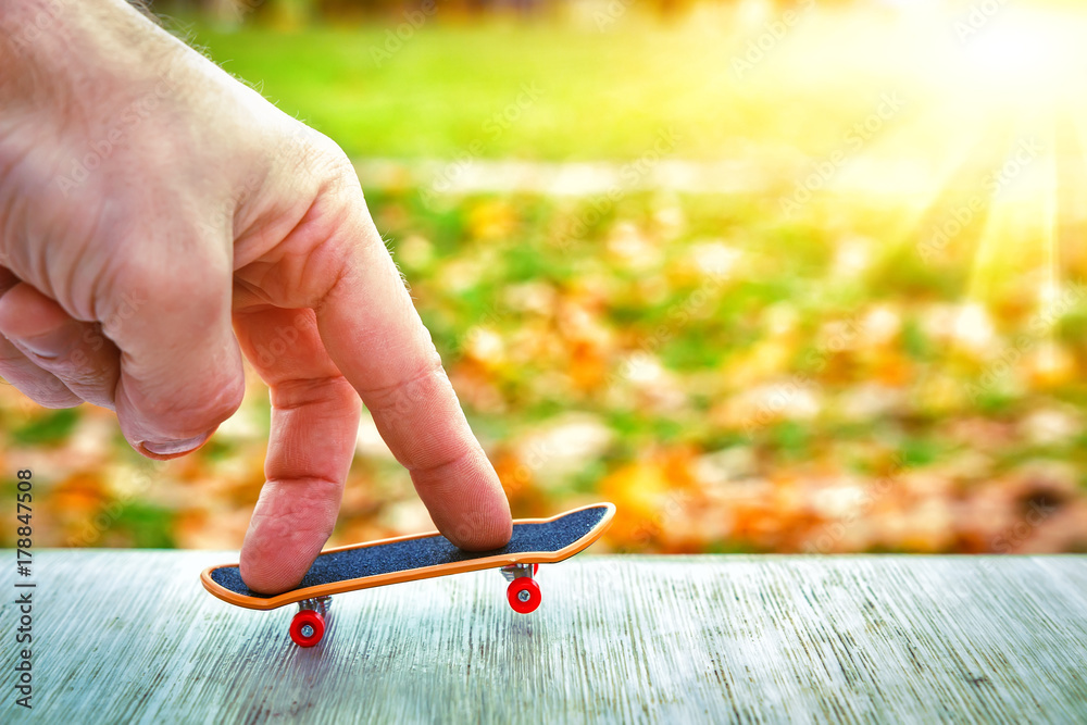 Fingers of hand skate on toy skateboard against green sunny background. concept of youth