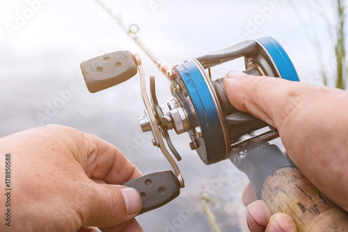 A man is fishing with a baitcasting  reel. Hands, a rod and a baitcasting reel photo