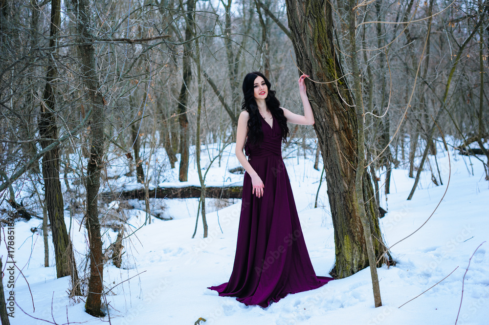 A young woman in an elegant burgundy evening dress in winter among trees and snow conceals a riddle A young woman in an elegant burgundy evening dress in winter among trees and snow conceals a riddle