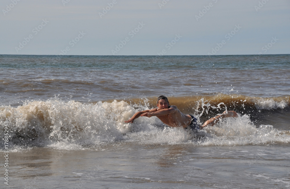A young man swims and having fun in the sea with a naked torso