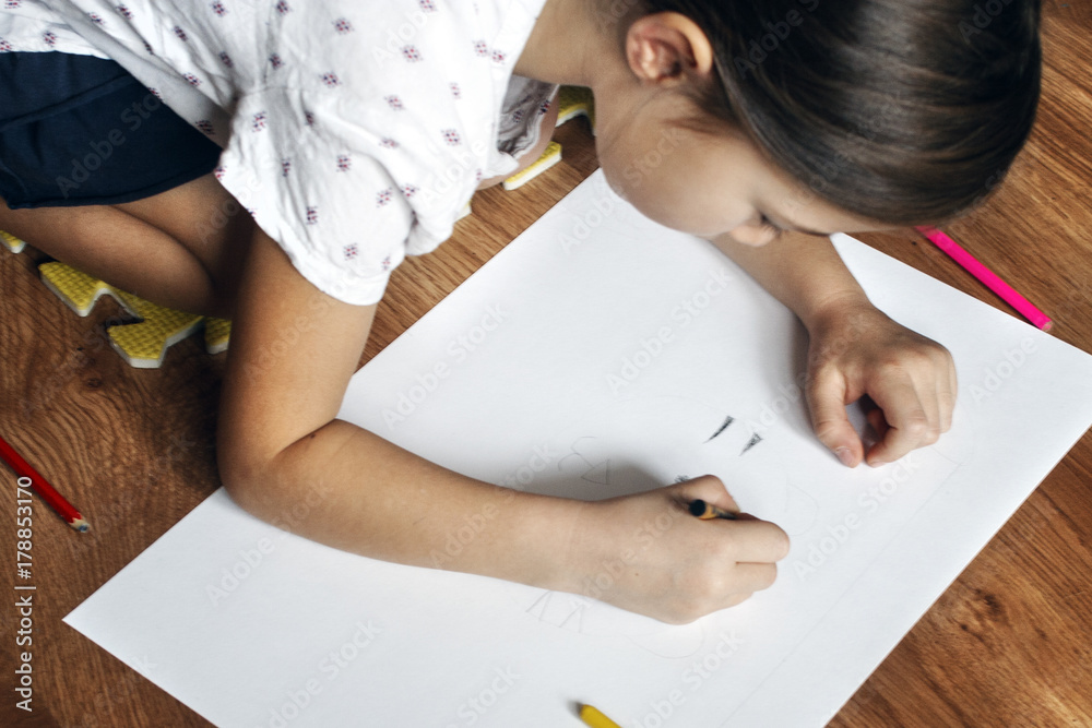 Girl draws picture with crayons on the sheet of paper on the floor Girl draws picture with crayons on the sheet of paper on the floor