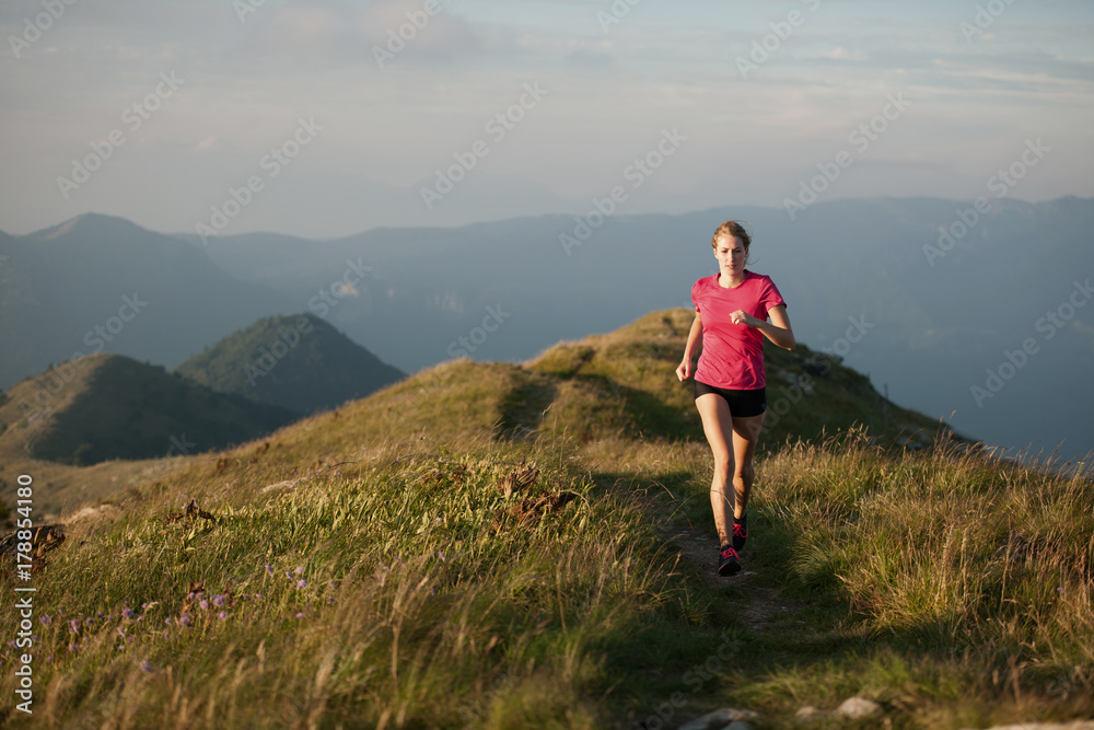 Woman runs on a top of the mountains with mountain range in background Woman runs on a top of the mountains with mountain range in background