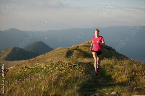 Woman runs on a top of the mountains with mountain range in background © Samo Trebizan