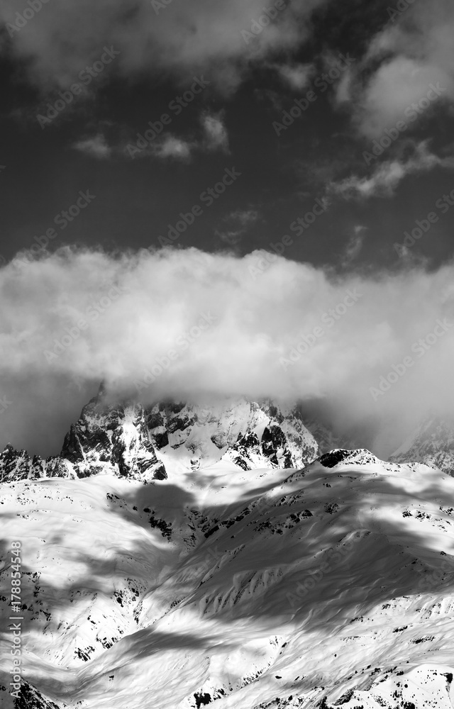 Black and white snow mountains in clouds at sun winter day