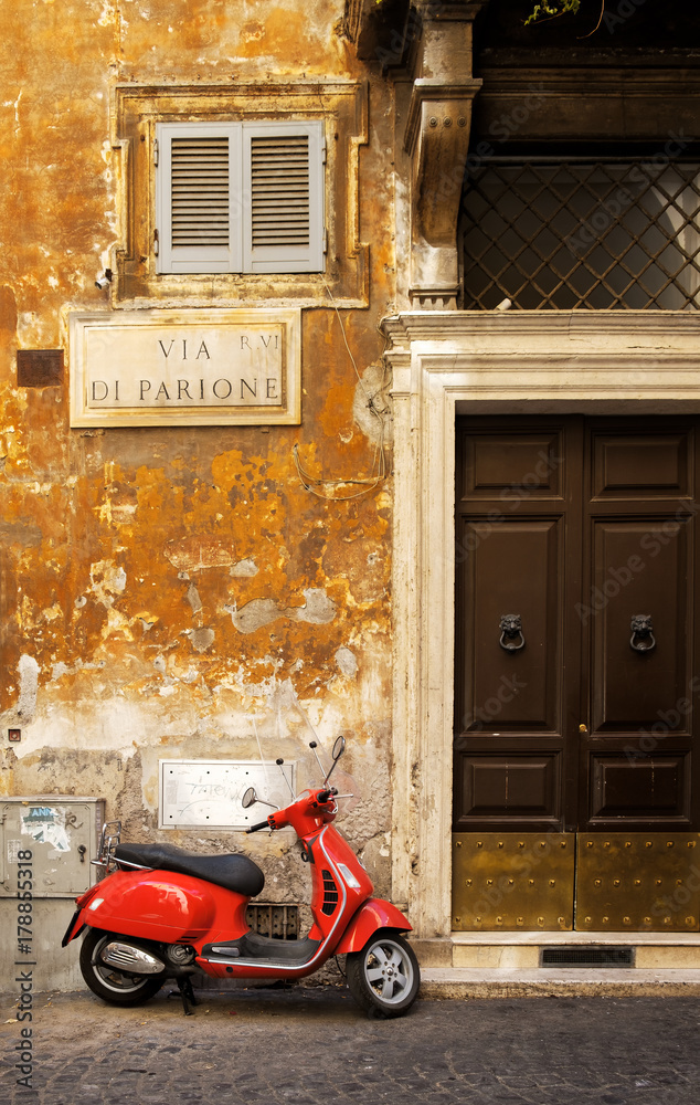Naklejka premium Wąska ulica w Rzymie z typowym czerwonym skuterem Vespa na brukowanej ulicy