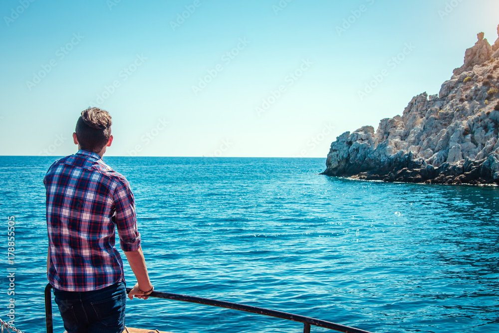 Fototapeta premium Young man enjoys the seaside view on a wooden yacht
