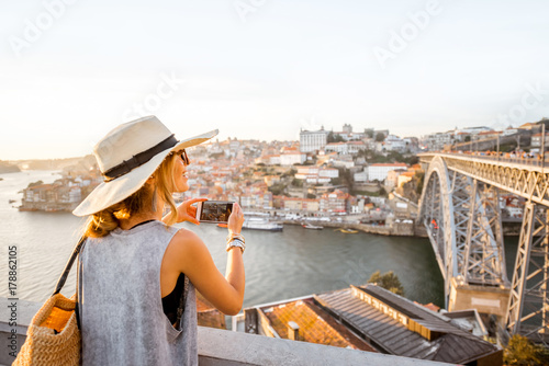 Young woman tourist photographing with phone beautiful landscape view on the old town with river and famous iron bridge in Porto city, Portugal
