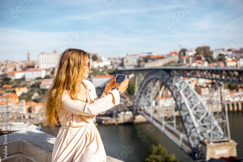 Young woman photographing with phone beautiful cityscape view with famous iron bridge in Porto city, Portugal © rh2010