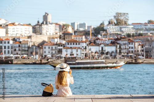 Young woman tourist sitting back on the Ribeira promenade enjoying cityscape view on the Porto city during the sunny day in Portugal